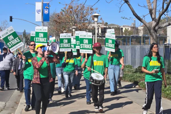 AFSCME Members in green shirts walking picket line with signs that say ON STRIKE.