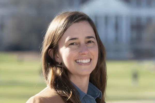 Photo of white woman with brown hair smiling and wearing a blue shirt and brown blazer
