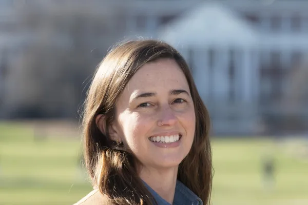 Photo of white woman with brown hair smiling and wearing a blue shirt and brown blazer