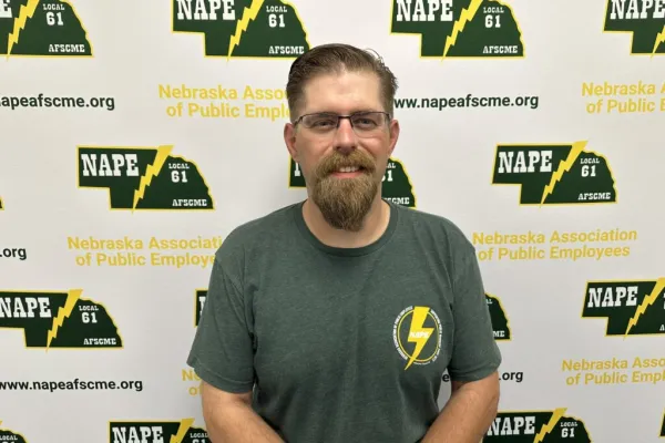 Photo of a white man with sandy blonde hair and beard in from of a NAPE AFSCME backdrop
