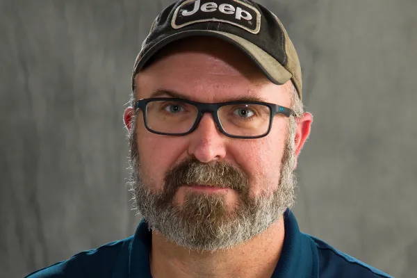 Photo of white man with salt and pepper beard wearing a ball cap and navy polo with University of Illinois logo