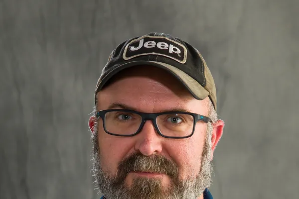 Photo of white man with salt and pepper beard wearing a ball cap and navy polo with University of Illinois logo