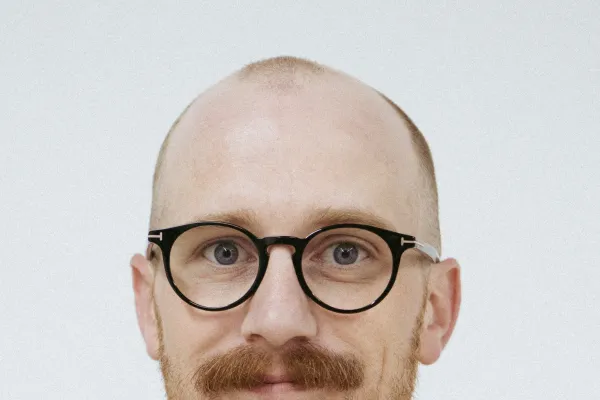 Photo of white man with trim reddish brown beard and glasses, wearing a dark blue shirt