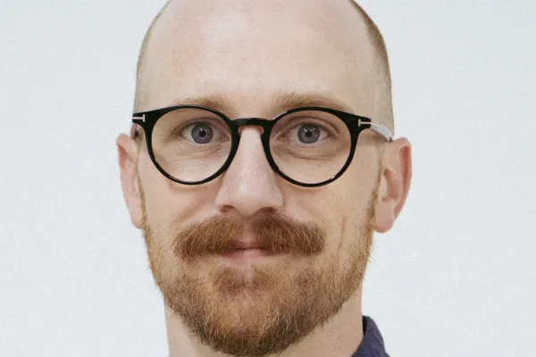 Photo of white man with trim reddish brown beard and glasses, wearing a dark blue shirt