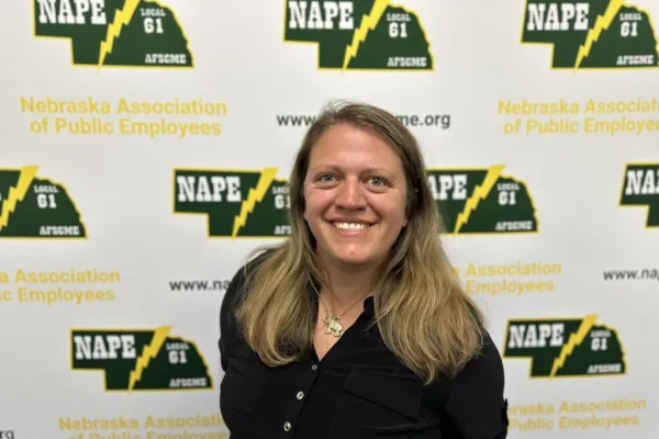 Photo of white woman with past shoulder length sandy blonde hair wearing a black shirt on a NAPE AFSCME background