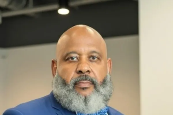 Photo of Black man with salt and pepper beard in a white shirt, blue blazer and blue printed bowtie