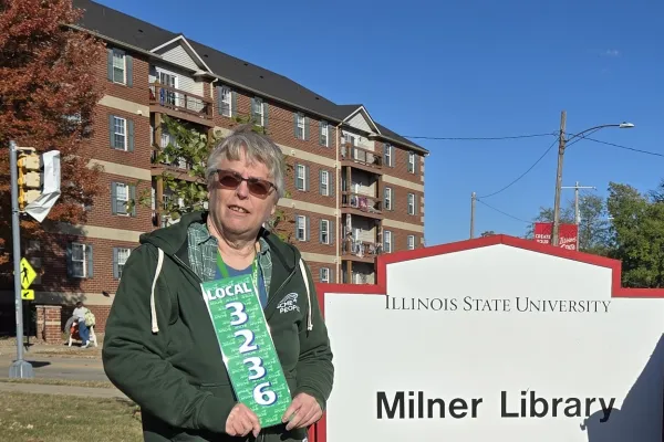 Photo of woman with short grey hair standing in front of Milner Library sign holding an AFSCME Local 3236 sign