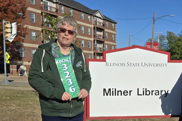 Photo of woman with short grey hair standing in front of Milner Library sign holding an AFSCME Local 3236 sign