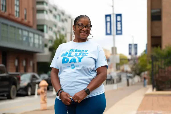 Photo of a Black woman in a white shirt with blue writing that says Tuesday Blues Day 