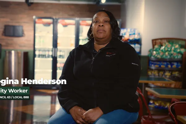 Photo of a Black woman in a black zip sweater in front of a background of a college cafeteria