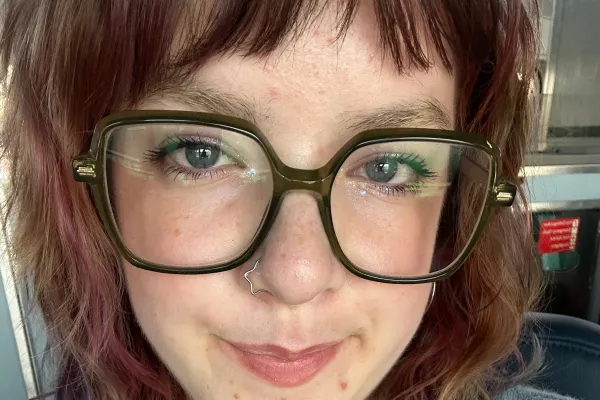 Photo of a white person with shoulder lenth hair and large black rimmed glasses