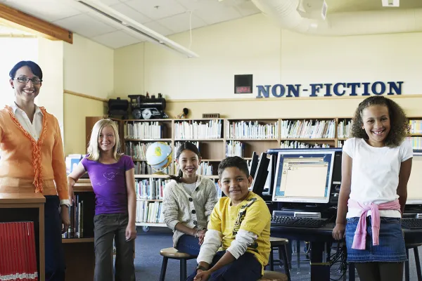 Photo of a teacher with school children in a library setting. Photo credit: Getty Images