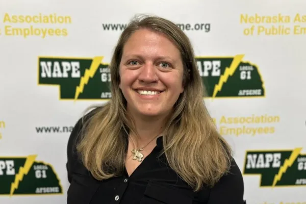 Photo of white woman with past shoulder length sandy blonde hair wearing a black shirt on a NAPE AFSCME background