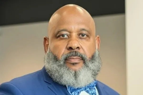 Photo of Black man with salt and pepper beard in a white shirt, blue blazer and blue printed bowtie
