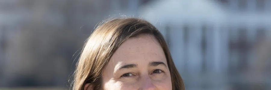 Photo of white woman with brown hair smiling and wearing a blue shirt and brown blazer