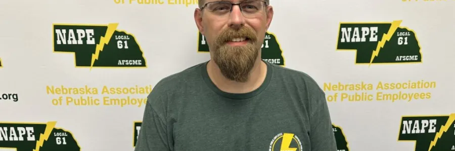 Photo of a white man with sandy blonde hair and beard in from of a NAPE AFSCME backdrop