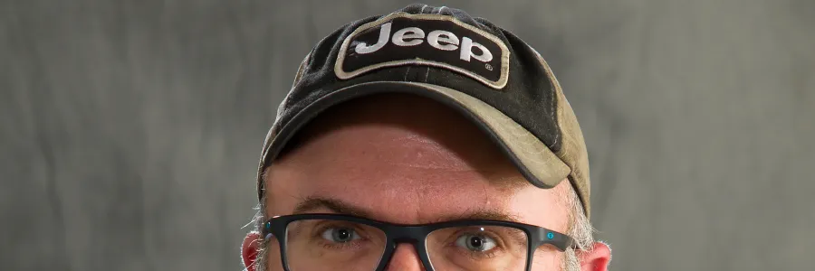 Photo of white man with salt and pepper beard wearing a ball cap and navy polo with University of Illinois logo