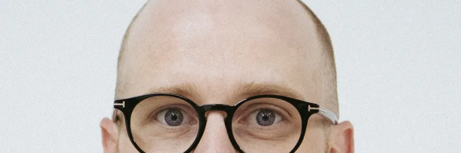 Photo of white man with trim reddish brown beard and glasses, wearing a dark blue shirt