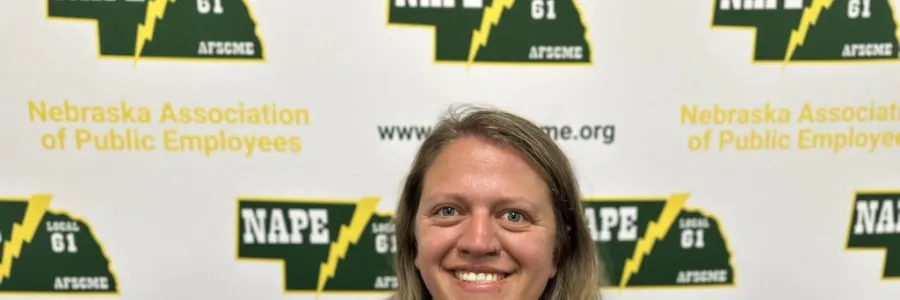 Photo of white woman with past shoulder length sandy blonde hair wearing a black shirt on a NAPE AFSCME background