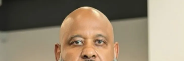 Photo of Black man with salt and pepper beard in a white shirt, blue blazer and blue printed bowtie