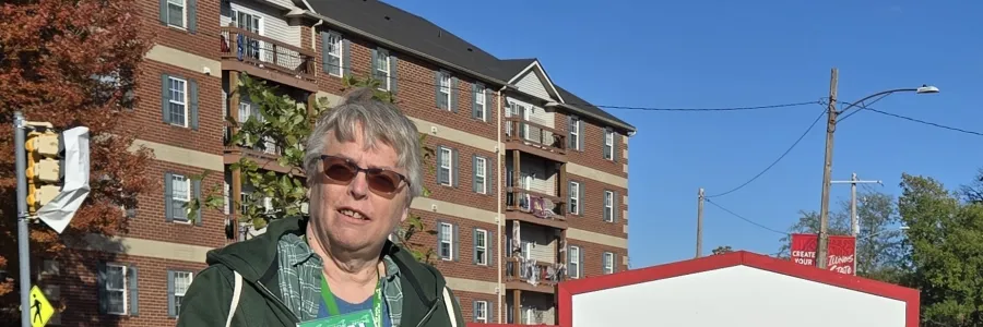Photo of woman with short grey hair standing in front of Milner Library sign holding an AFSCME Local 3236 sign