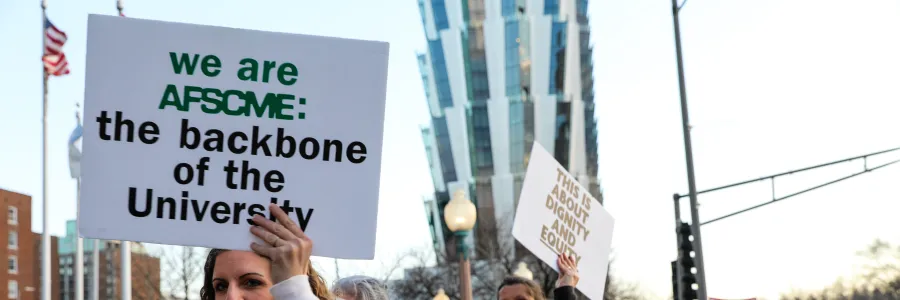 Photo of a woman with a sign that says "We are AFSCME: the backbone of the University"