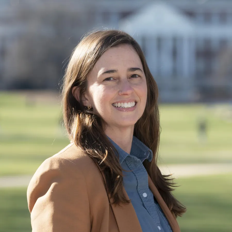 Photo of white woman with brown hair smiling and wearing a blue shirt and brown blazer