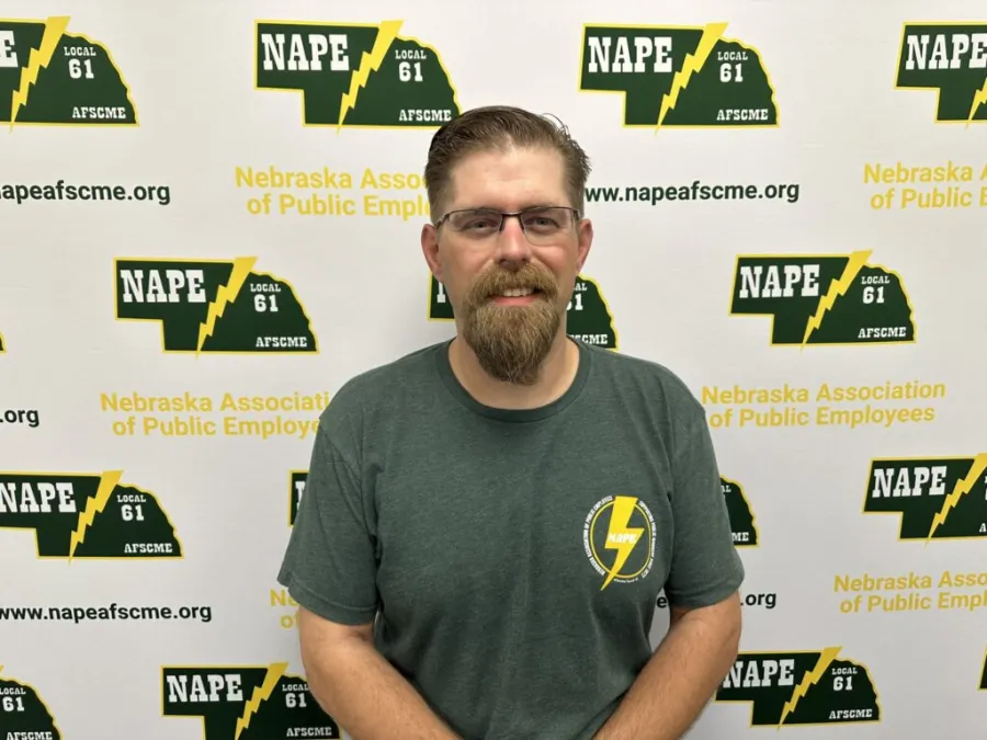 Photo of a white man with sandy blonde hair and beard in from of a NAPE AFSCME backdrop