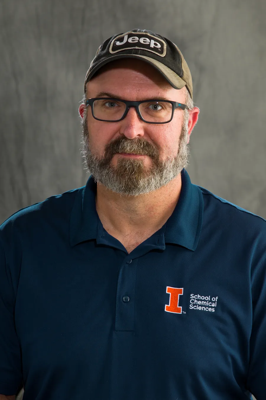 Photo of white man with salt and pepper beard wearing a ball cap and navy polo with University of Illinois logo