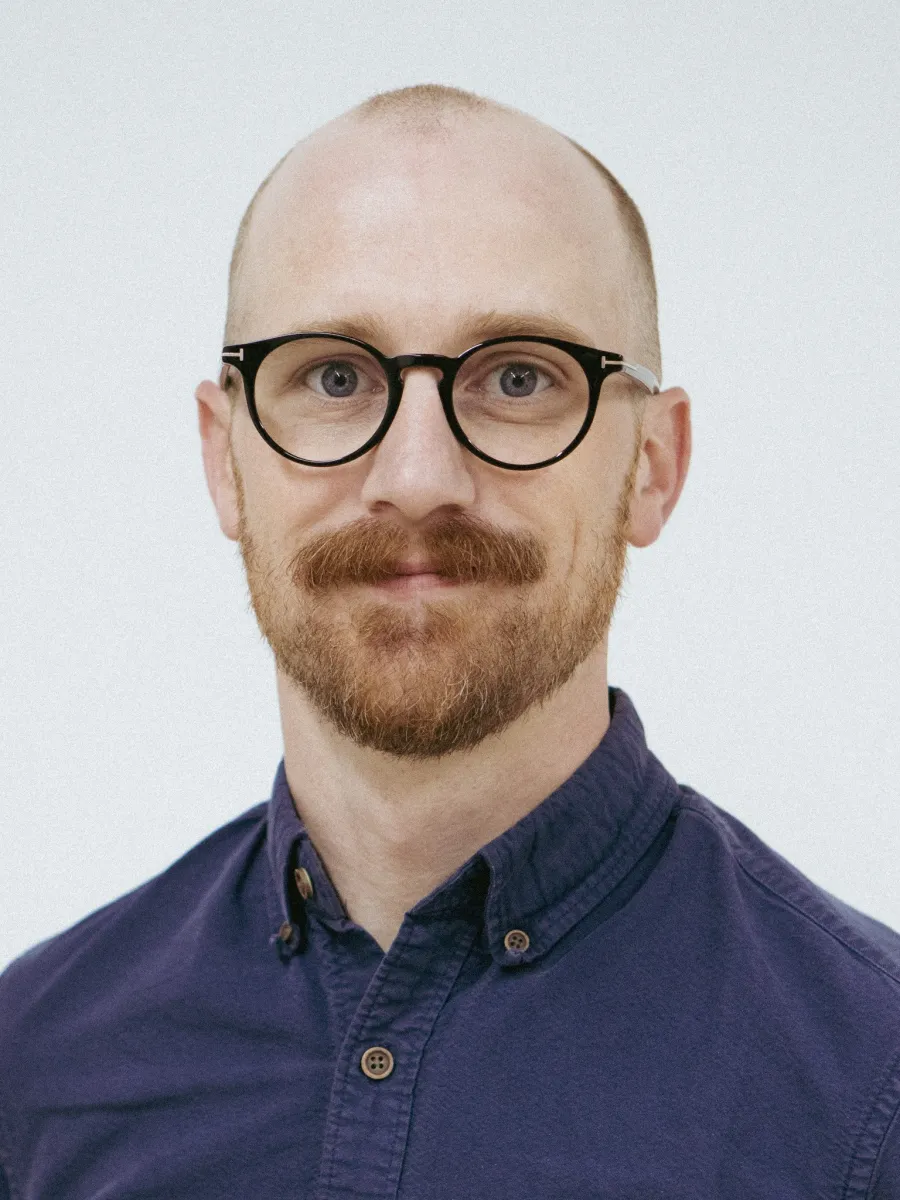 Photo of white man with trim reddish brown beard and glasses, wearing a dark blue shirt