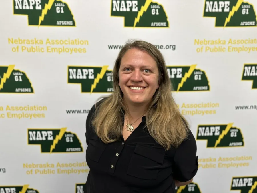 Photo of white woman with past shoulder length sandy blonde hair wearing a black shirt on a NAPE AFSCME background