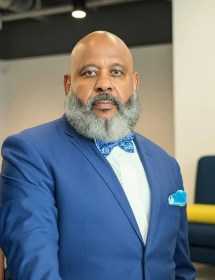 Photo of Black man with salt and pepper beard in a white shirt, blue blazer and blue printed bowtie