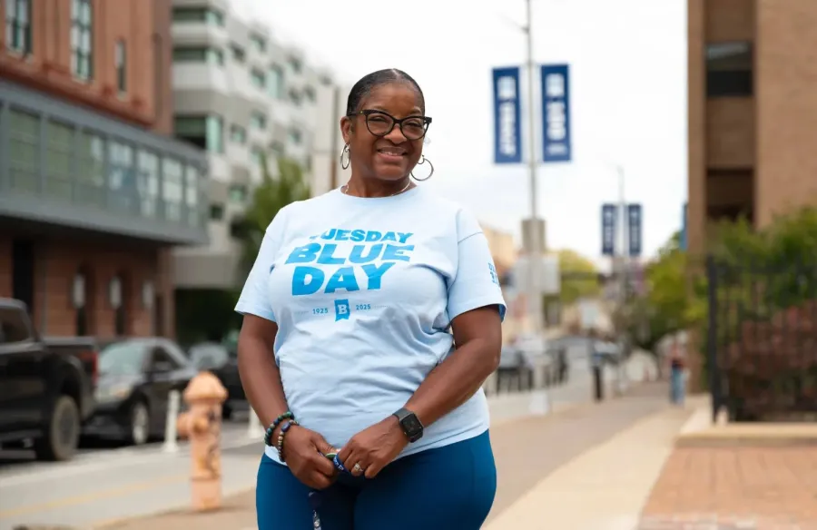 Photo of a Black woman in a white shirt with blue writing that says Tuesday Blues Day 