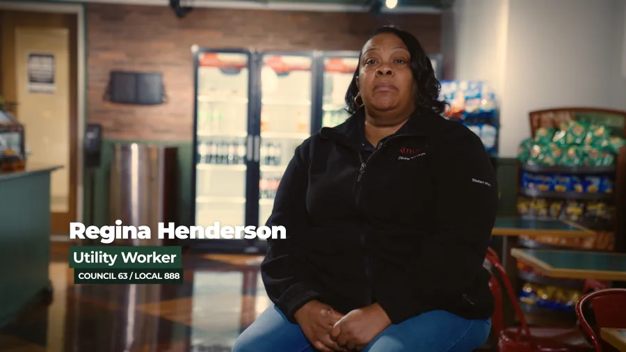 Photo of a Black woman in a black zip sweater in front of a background of a college cafeteria
