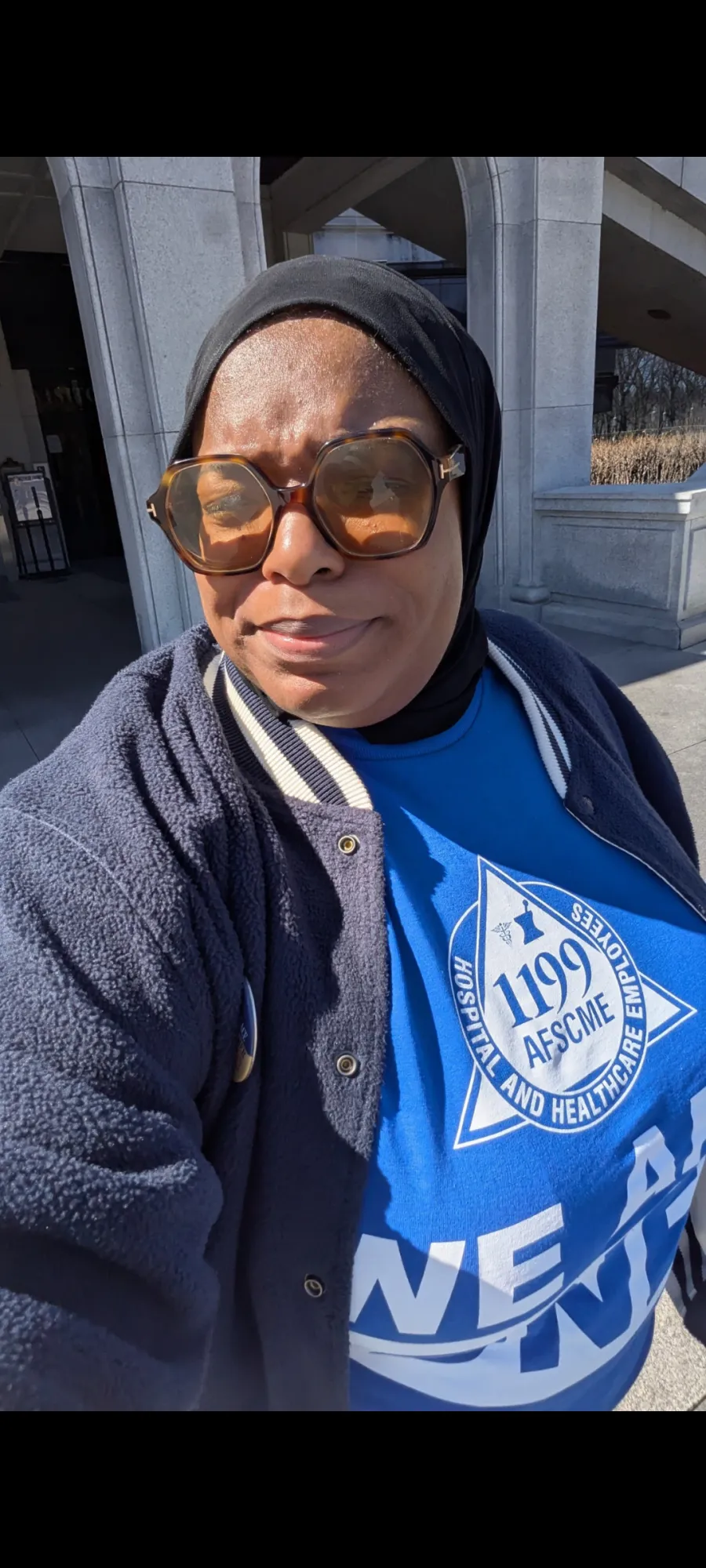 Selfie photo of a Black woman with a blue 1199 AFSCME shirt on