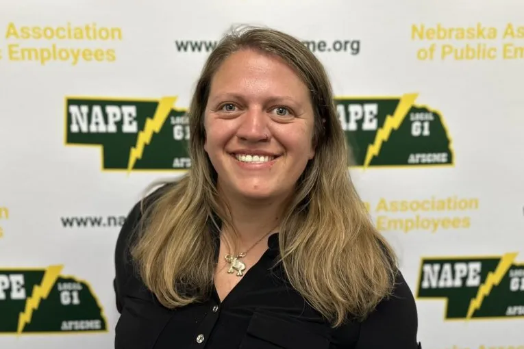 Photo of white woman with past shoulder length sandy blonde hair wearing a black shirt on a NAPE AFSCME background